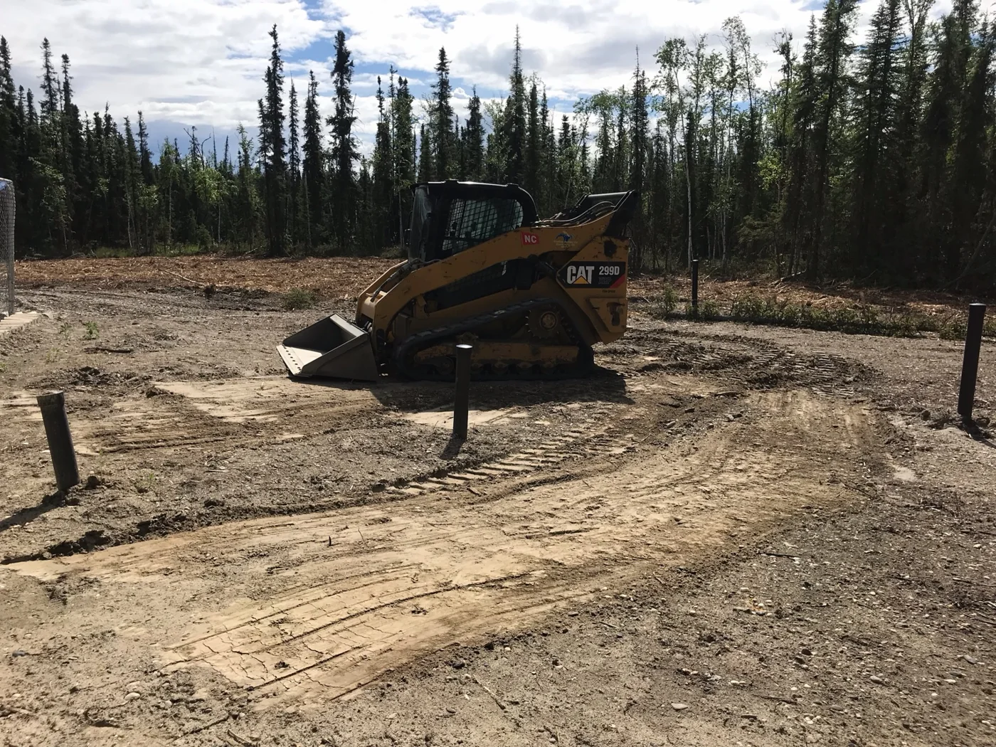 Compact track loader on a cleared dirt work site bordered by trees