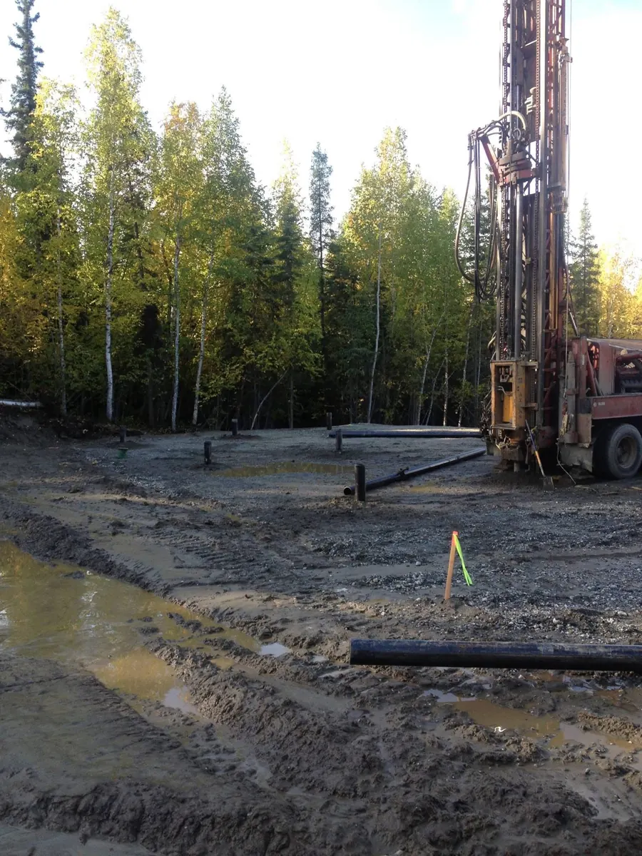 Truck-mounted well drilling rig with pipe laid across a cleared site surrounded by trees