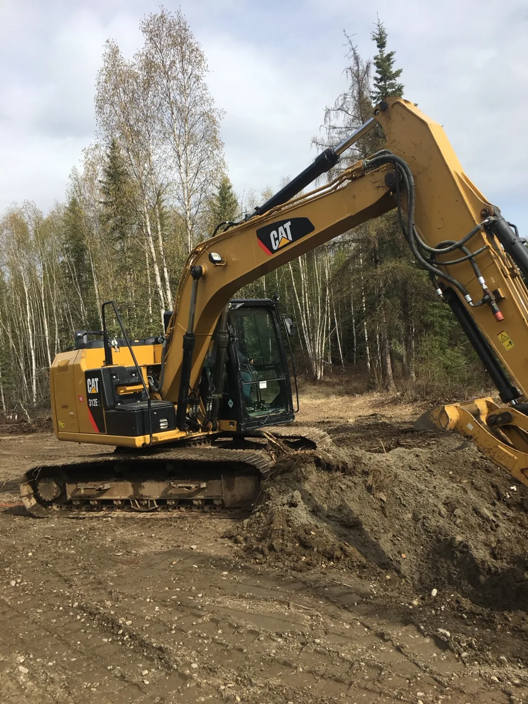 Tracked excavator moving soil on a wooded dirt work site