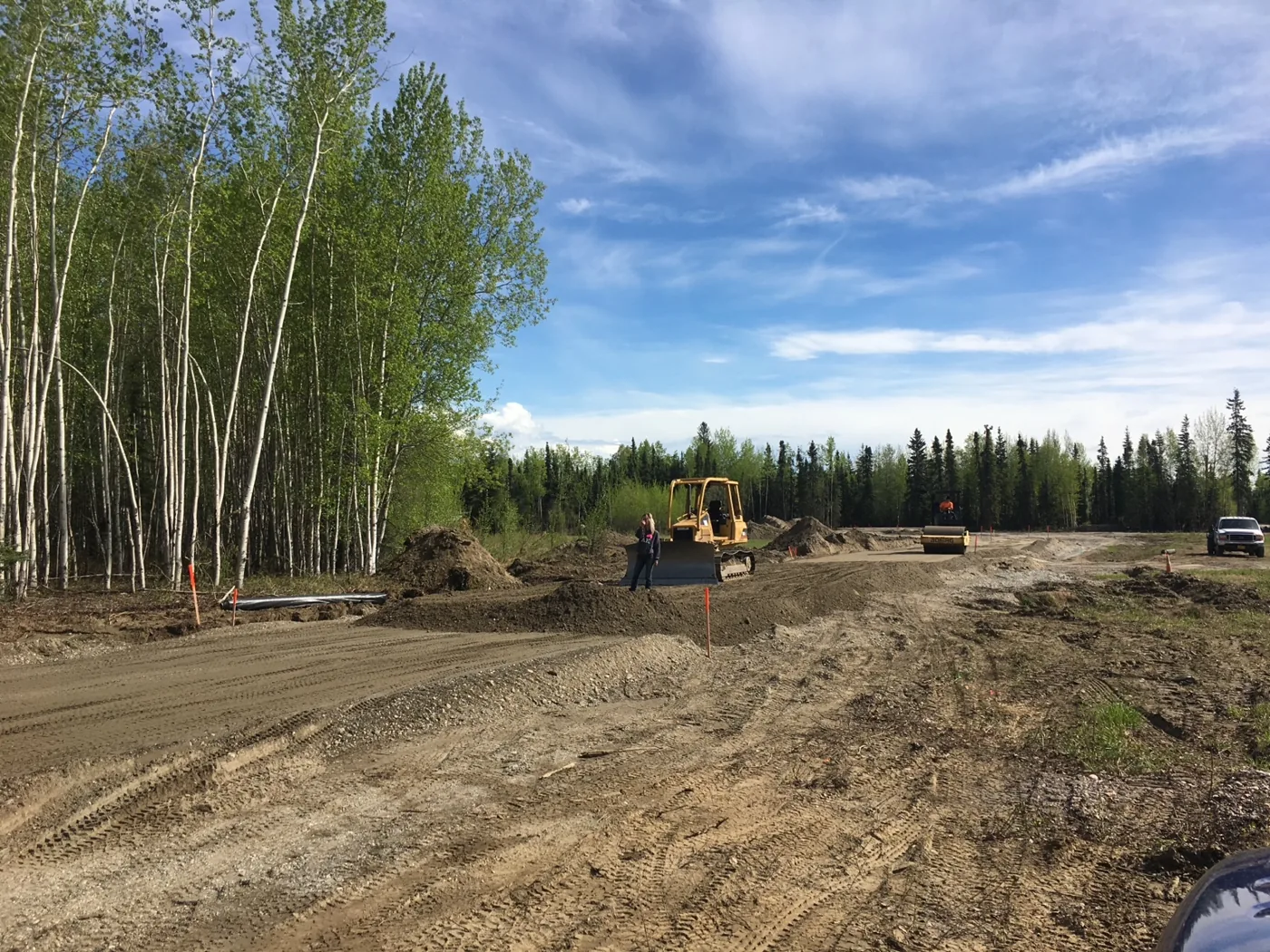 Graded dirt work area with heavy equipment and trees beneath a blue sky