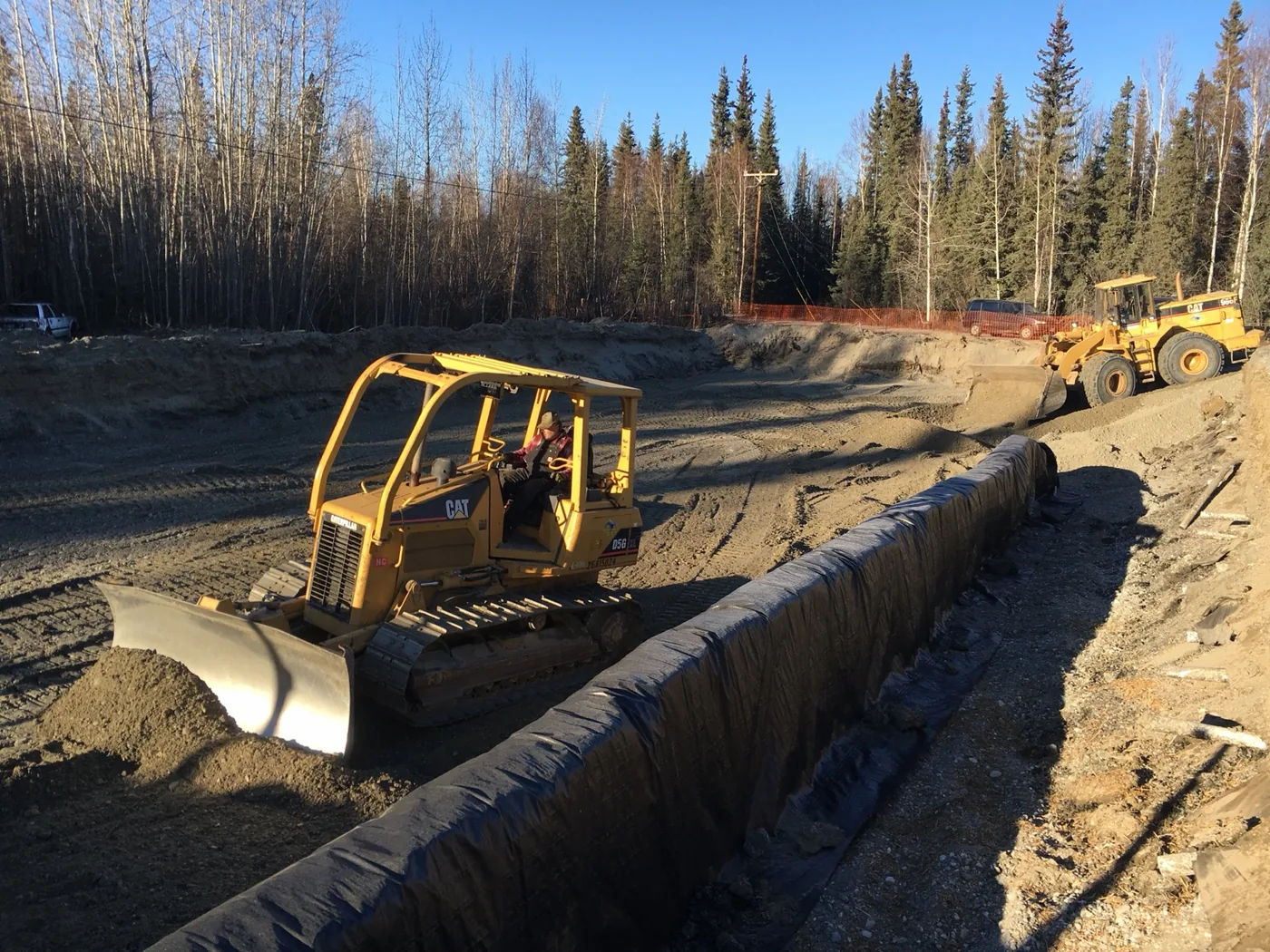 Dozer beside a long lined excavation at a dirt work site