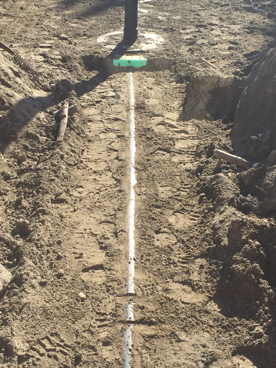 Excavated trench with a white pipe and green cap
