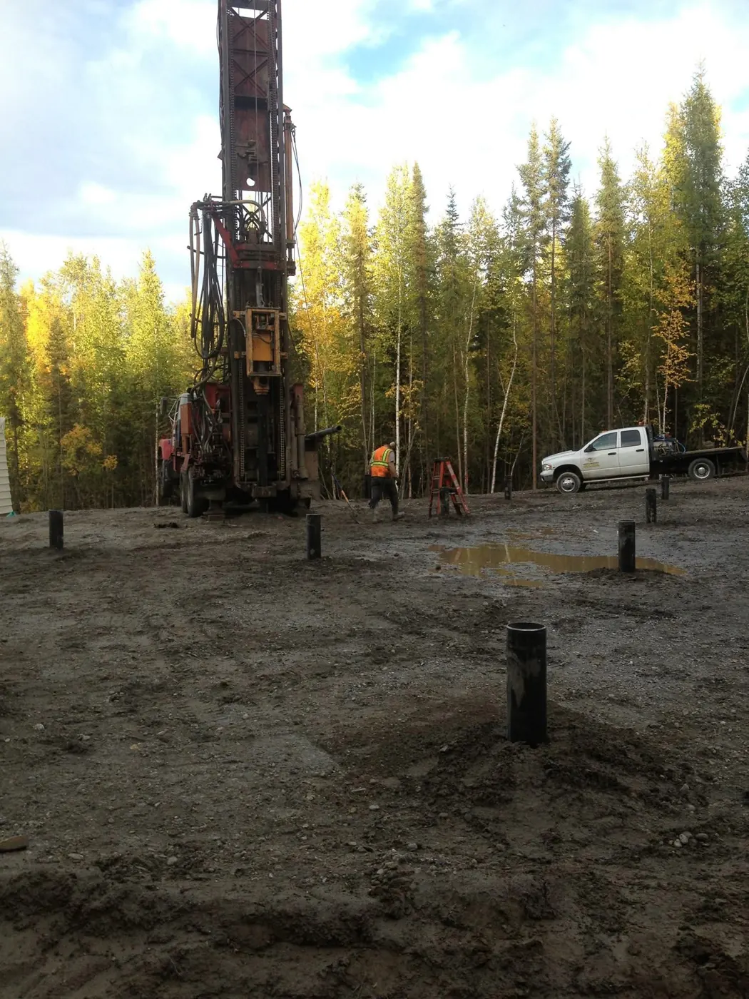 Water well drilling rig and crew beside a work truck at a wooded job site